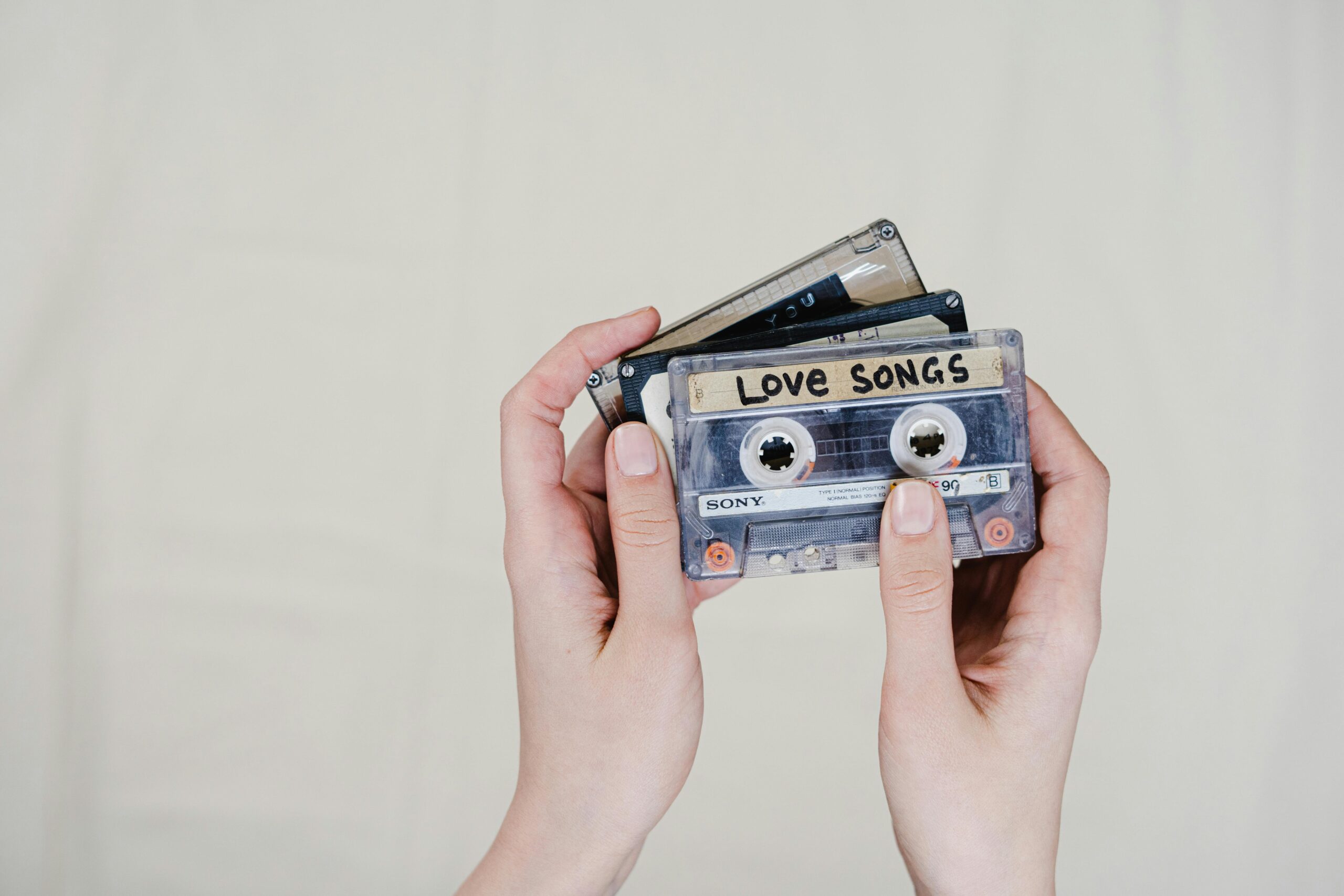 Hands hold a stack of old cassette tapes, with the front one labeled "Love Songs."