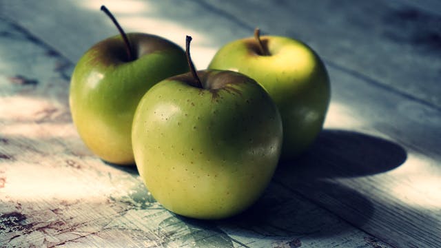 three green apples on a table