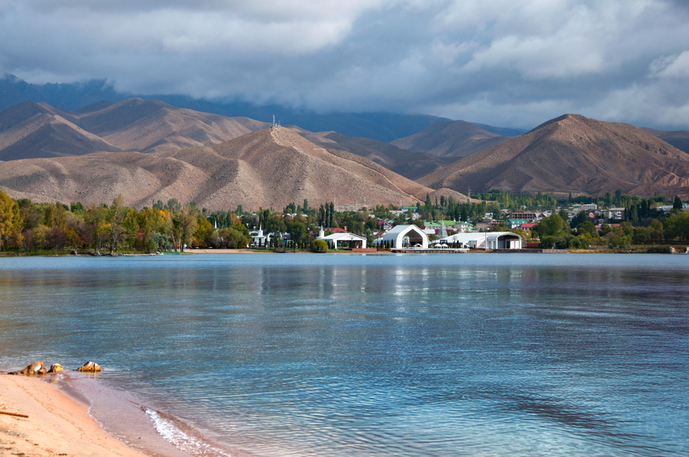 Beautiful clear blue water of Issyk-Kul lake near Cholpon-Ata city with view over Ruh Ordo cultural complex with dramatic grey heavy clouds, Kyrgyzstan landscape