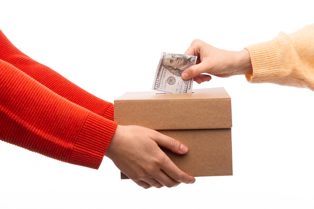 charity, savings and fundraising concept - close up of hand putting dollar cash money into donation box