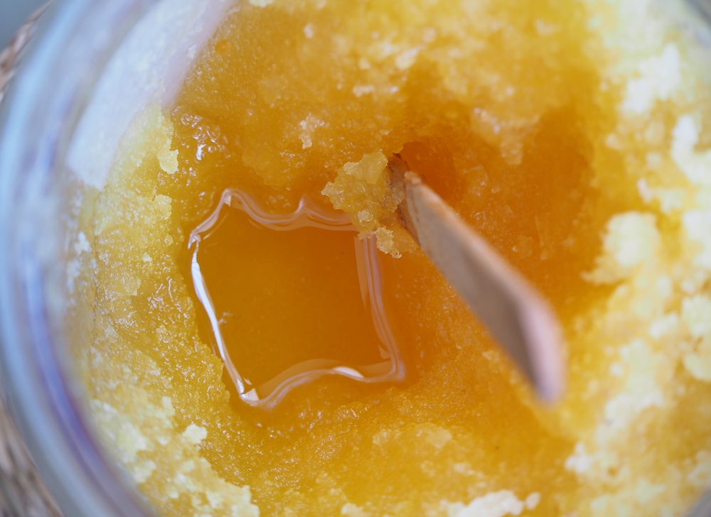 Crystallized honey and wooden stick in a glass jar. Selected focus.