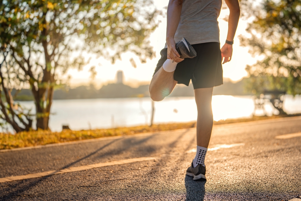 Man runner stretching leg and feet and preparing for jogging and running in public park outdoors at sunset, Active and healthy lifestyle concept.