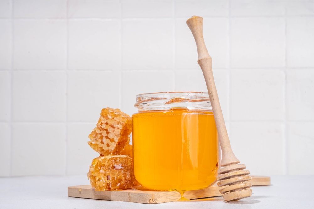 Golden flower honey in a small jar, with honey spoon and honeycomb