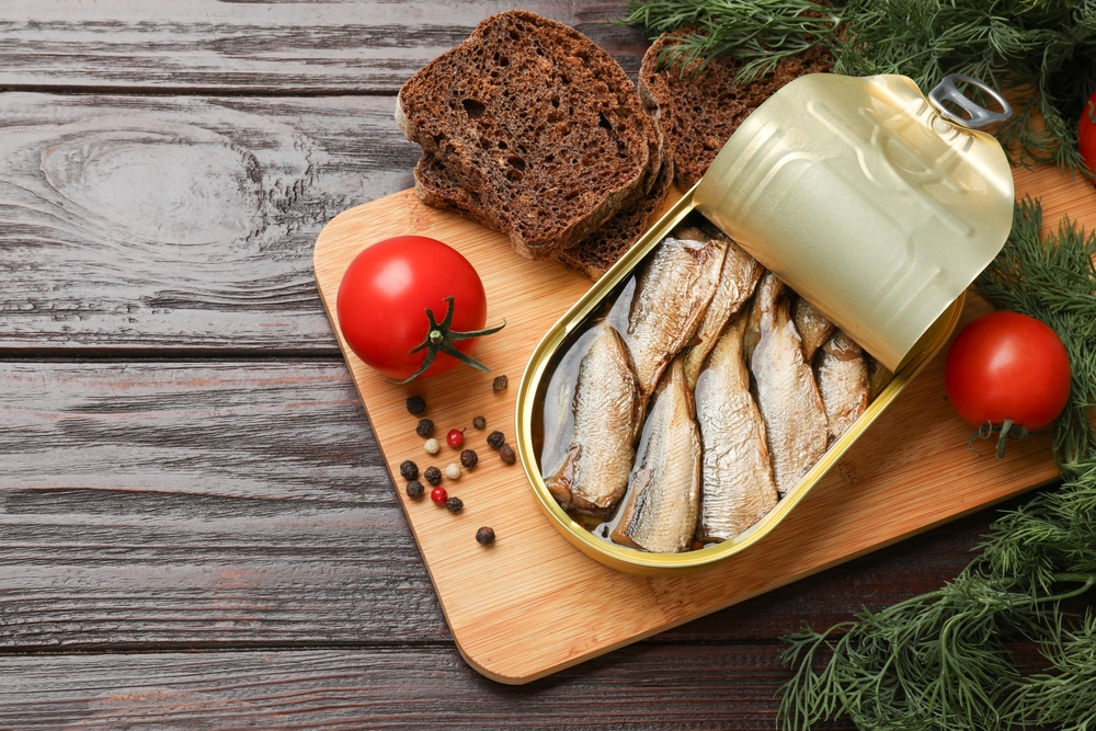 Tasty sprats in tin can served on wooden table, flat lay