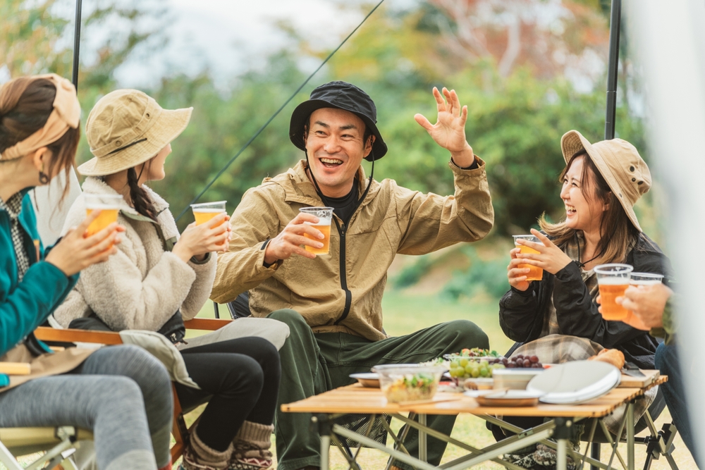 A popular Asian man drinking beer and telling jokes with his friends at a campsite in autumn and winter