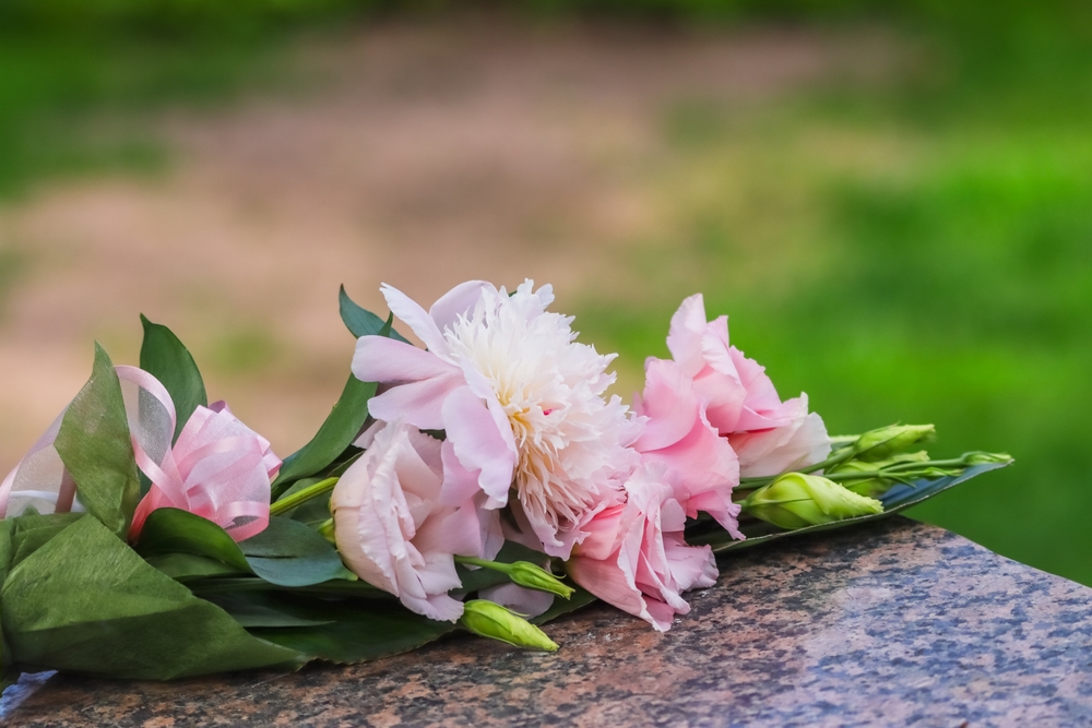 Single bouquet of flowers on a cemetery memorial stone. Beautiful bouquet of pink flowers tied with a decorative ribbon. Empty space for text.