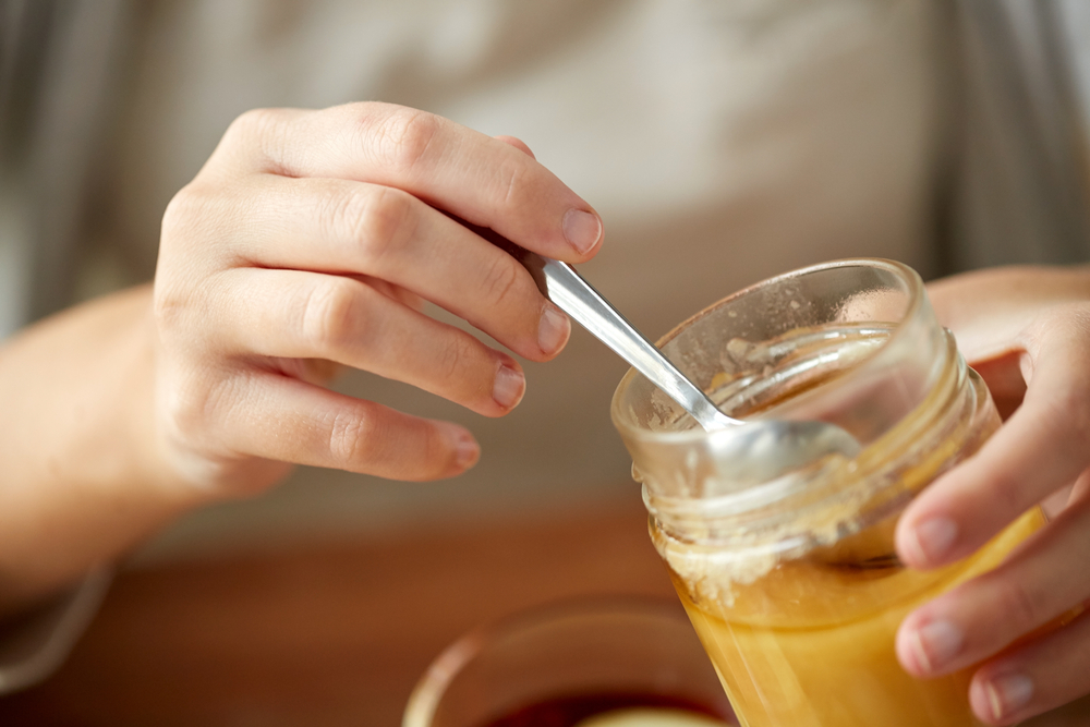 Garlic with honey in a glass jar on the kitchen counter with a wooden honey stick.