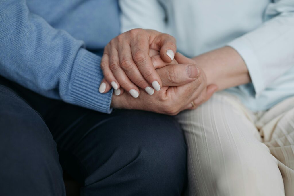 Two people holding hands tenderly, one wearing a blue sweater and the other in white.