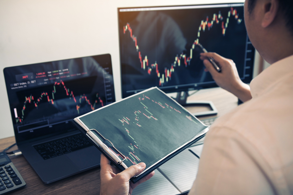 Investor man analyzing the graph of the stock market using a pen pointing to the computer screen.