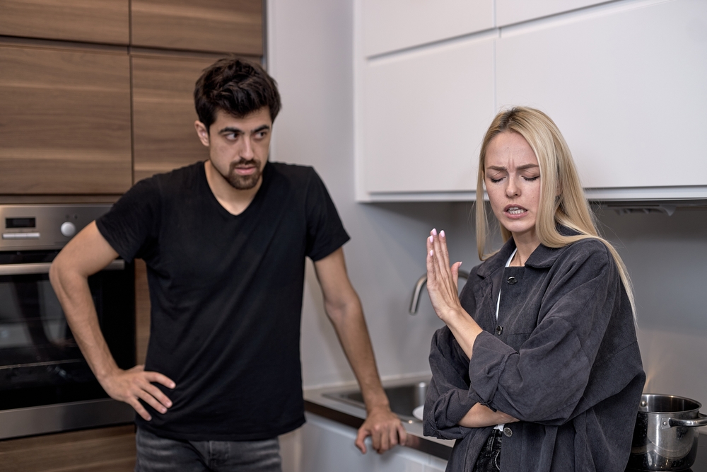 Angry married couple having quarrel, yelling at each other in kitchen. blonde young female is gesturing. Furious woman shouting at husband or boyfriend. Breaking up and divorce concept