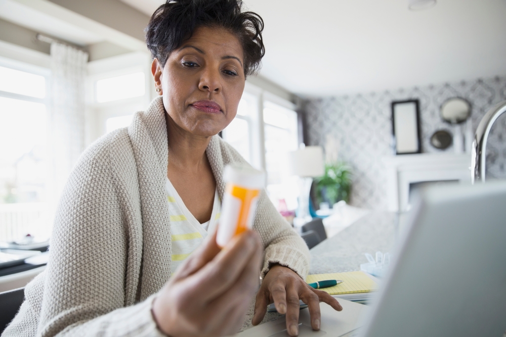 Woman reading prescription bottle label at laptop