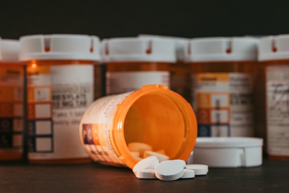white pills coming out of prescription pill bottle on black background