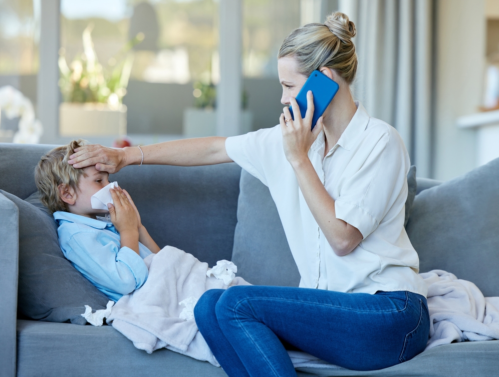 Phone call, kid and mom checking for fever with flu, cold or allergy on sofa at home. Sick, medical emergency and mother feel head of child for high temperature with telehealth consultation at house.