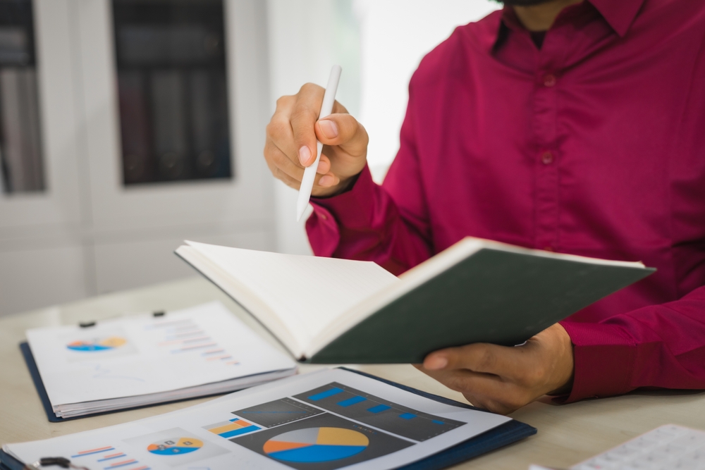 A focused man works diligently in his office, reviewing numerous accounting documents on his desk. His goal is to ensure accuracy and precision, avoiding errors in critical financial data.