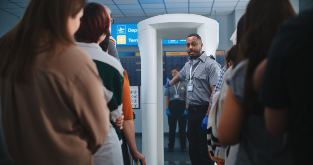 Airport Security Checkpoint: African American Security Officer Instructs Diverse People, Passengers About Metal Detector Scanner Gates, TSA Screening Procedures. Queue of Travelers Going on Trips.