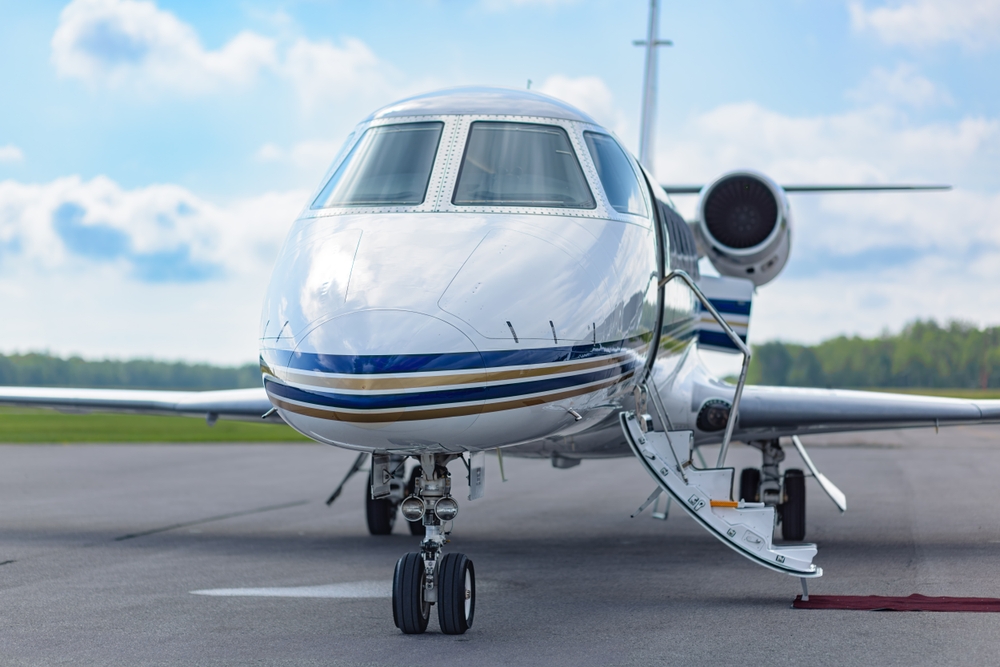 Boarding stairs of a private jet extend to the ground, inviting passengers into the cabin. The clean fuselage and turbine reflect the midday sky.