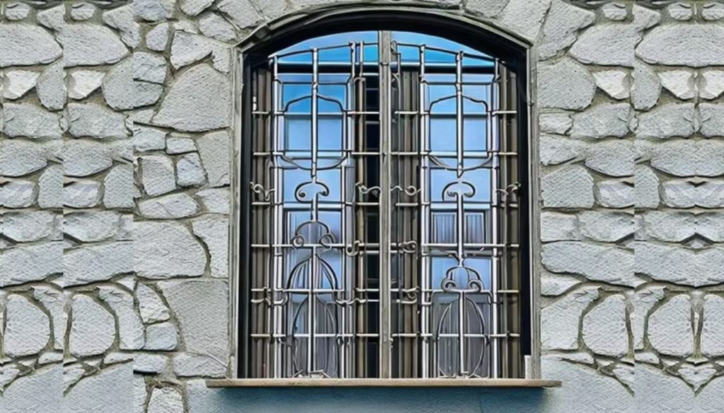 Intricate circular designed window grill on a window. Stone wall in the background.