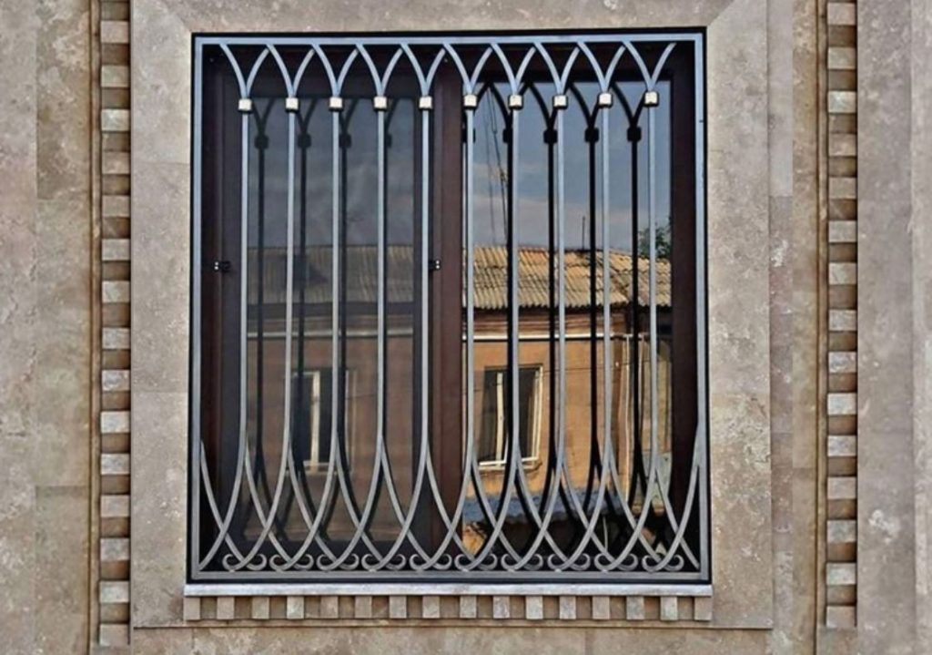Art deco style window grill. Stone wall and window reflecting a building in the background.