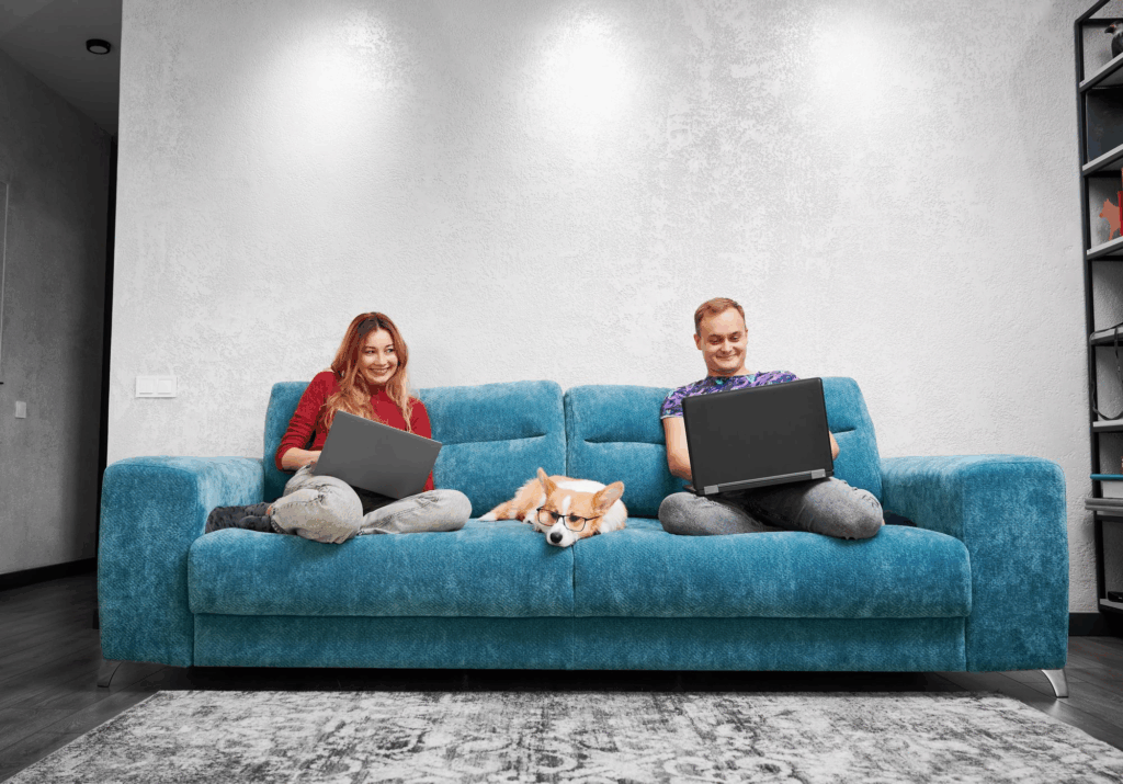 Married couple having fun using laptops at home sitting on couch