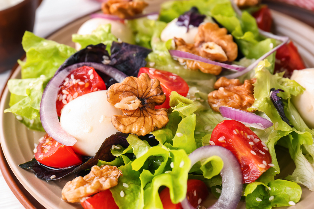 Delicious fresh salad with walnuts on plate, closeup