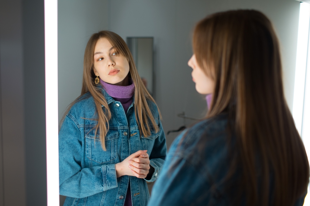 Young woman try on clothes in dressing room with mirror in shop.