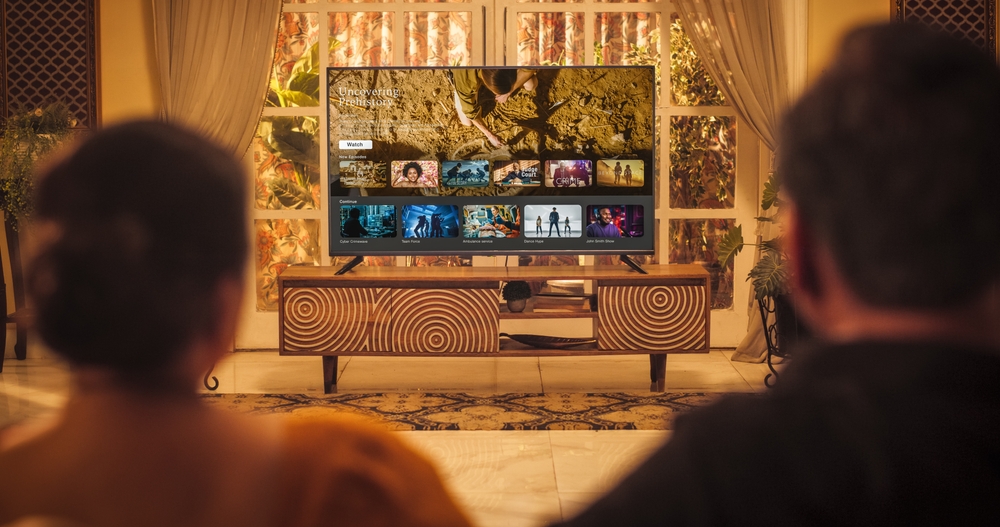 Back View of Elderly Indian Couple Watching TV while Sitting on a Couch in the Living Room. Relaxed Evening for Enjoying Favourite Movies, TV Shows, Content and Ads Thank to Streaming Online Service