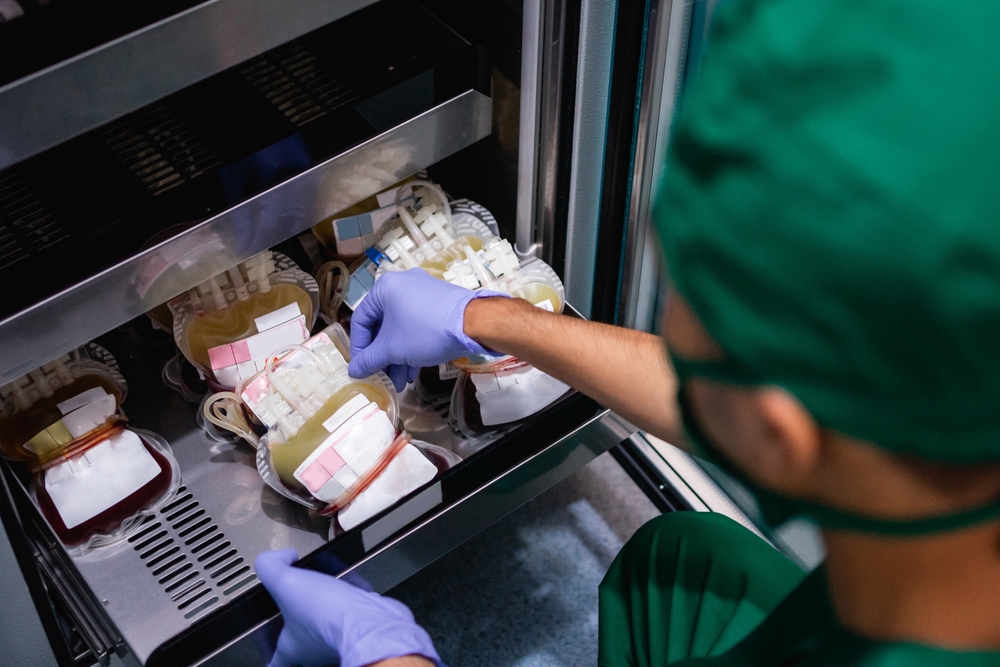 hand with rubber glove removing blood bag from stock in storage cabinet
