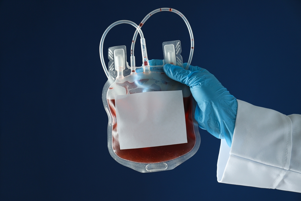 Bag with donor blood in gloved hand on blue background