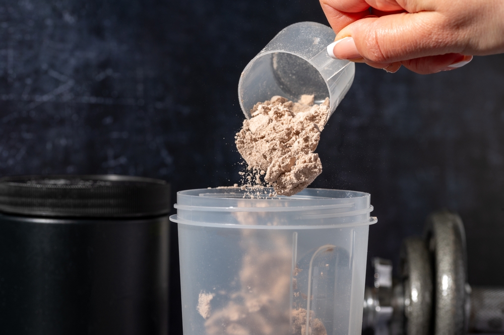pouring chocolate protein powder in a shaker. Food supplements. Dark background. Bodybuilding, fitness, gym.
