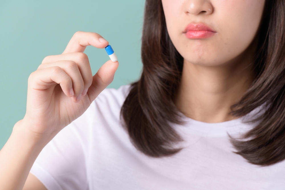 Forget taking medicine. Confused woman holds head and looks at pills on green background. Asian woman forget to take medicine, miss medication dose, and think of next prescription with a pill in hand.