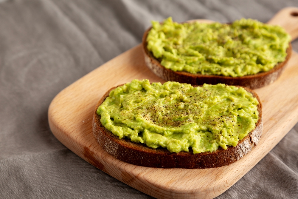 Homemade Avocado Toast with Salt and Pepper on a wooden board, side view.