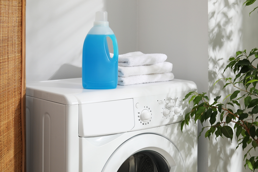 Bottle of fabric softener and towels on washing machine indoors