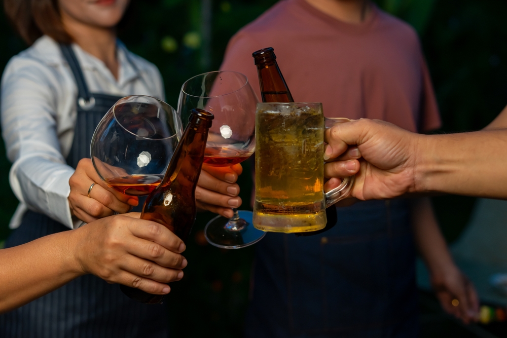People toasting with beer bottles and wine glasses at casual gathering