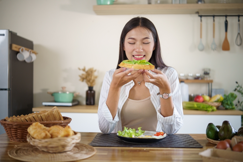 Young woman enjoying a healthy avocado toast breakfast in a cozy kitchen.