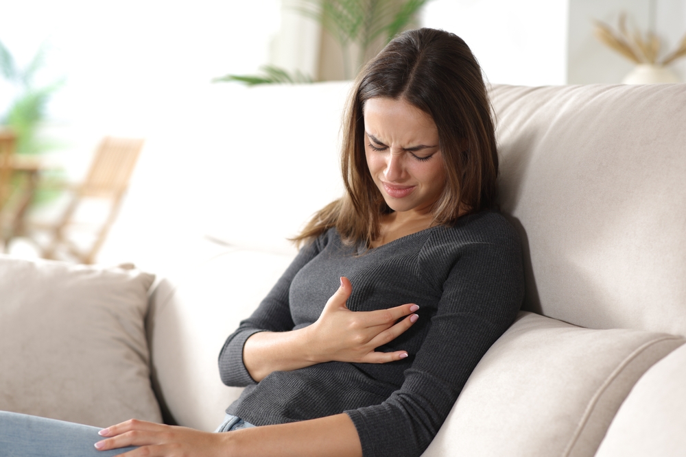Stressed woman suffering breast ache sitting on a couch at home
