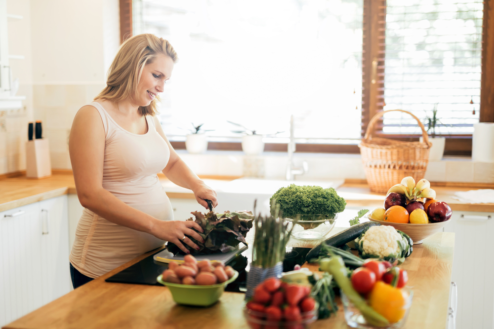 Beautiful pregnant woman preparing meal on kitchen island from fresh ingredients