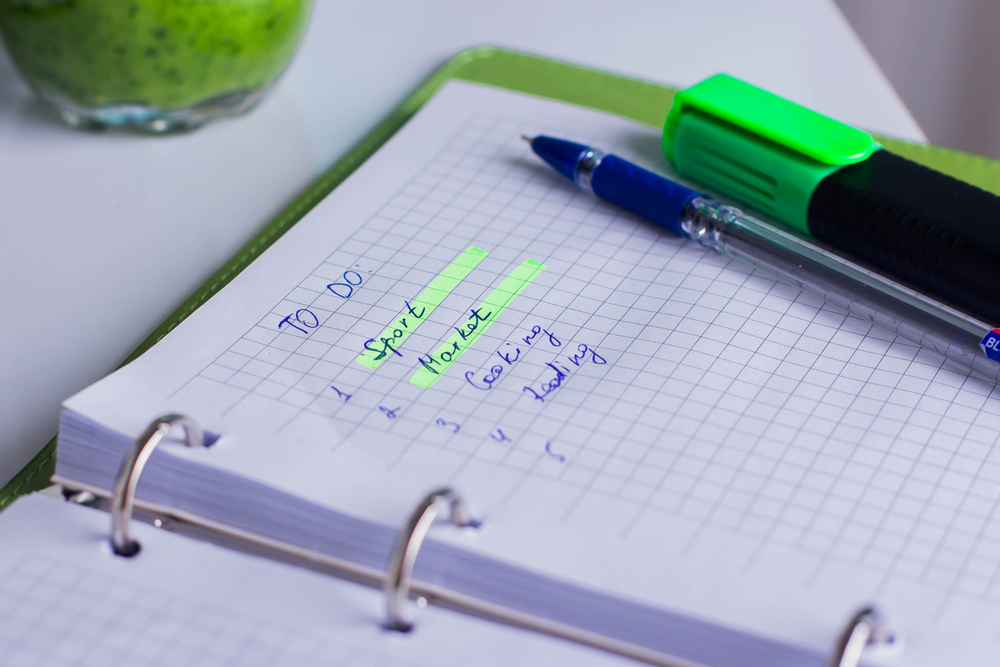 Notebook with to do list for housewife - Sport, Market, Cooking and Reading. Planning for day. Workplace of feelancer green smoothie for snack, notebook with action plan and pen, marker on white table