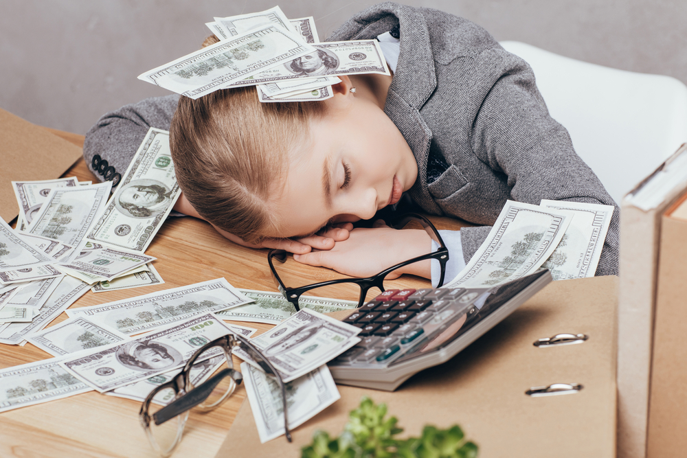 little girl in suit sleeping under pile of money at workplace isolated on grey