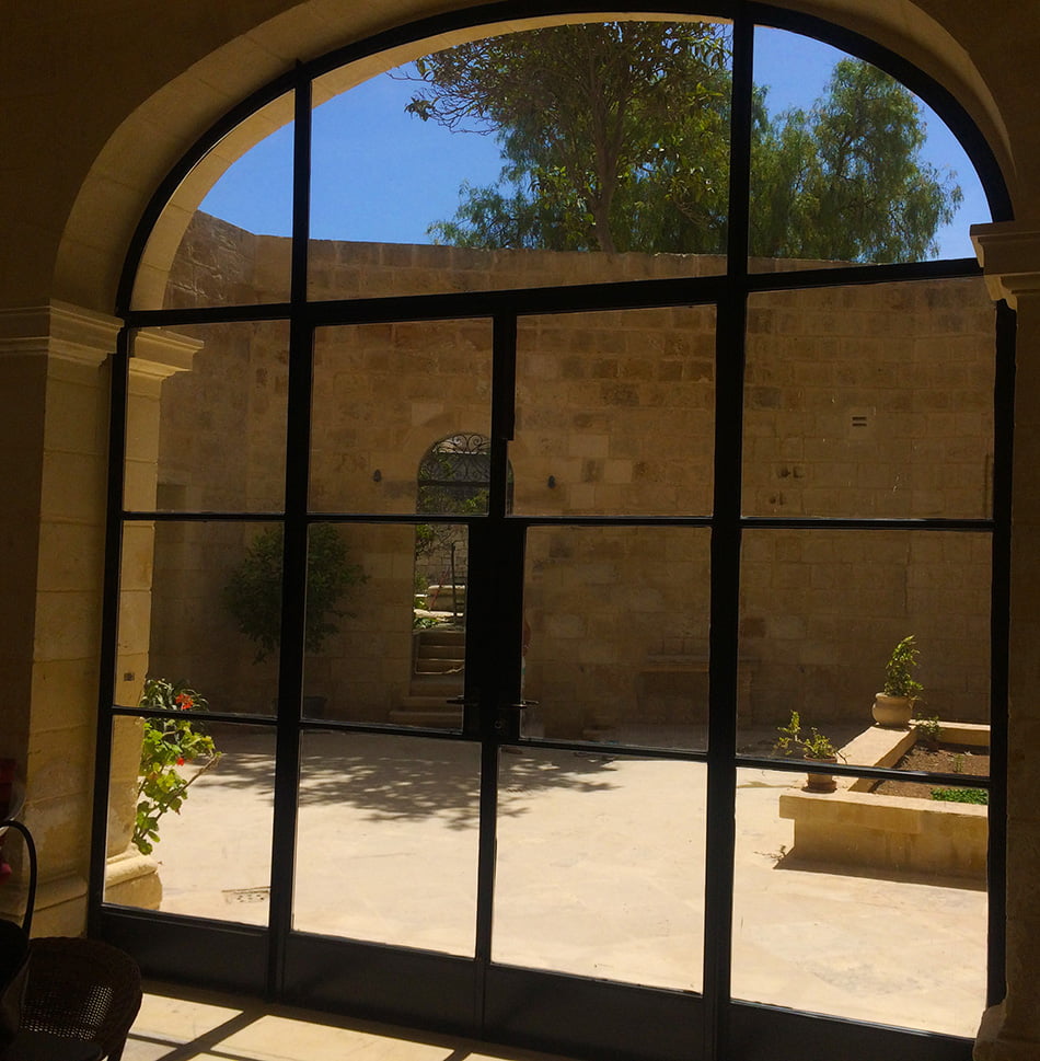 A glass door with panes. A backyard with stones a garden bed, and greenery. Brick wall in the background.