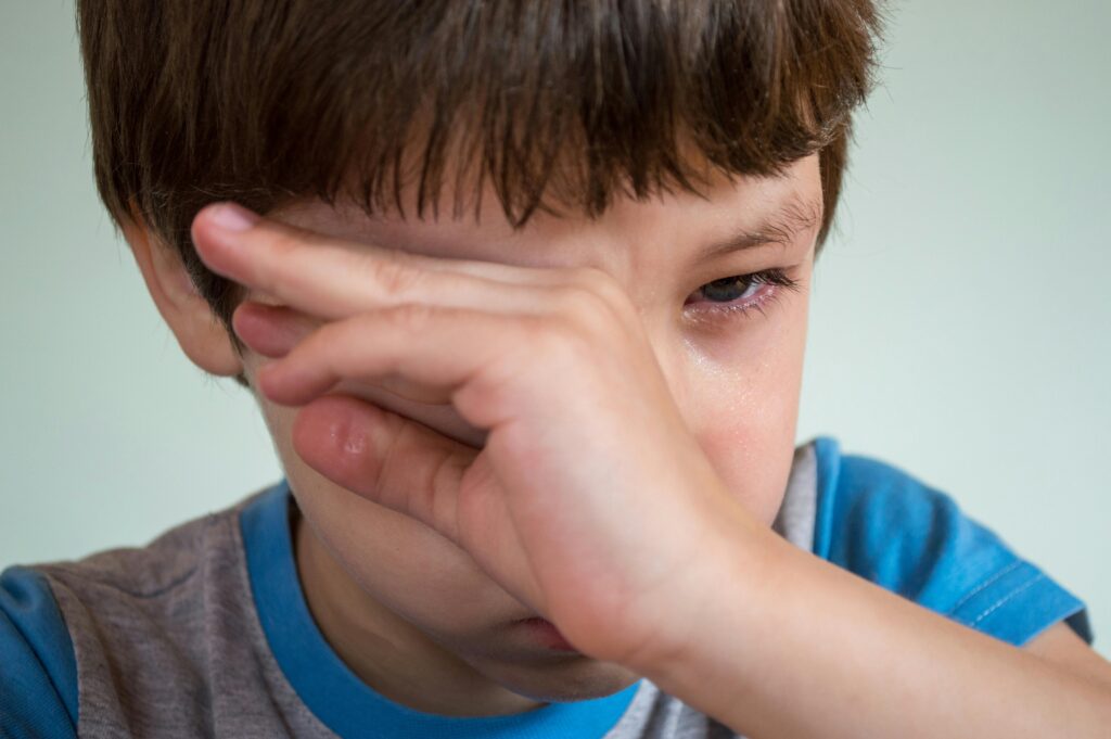 A young boy in a blue shirt rubs his eyes, appearing to be crying or upset.