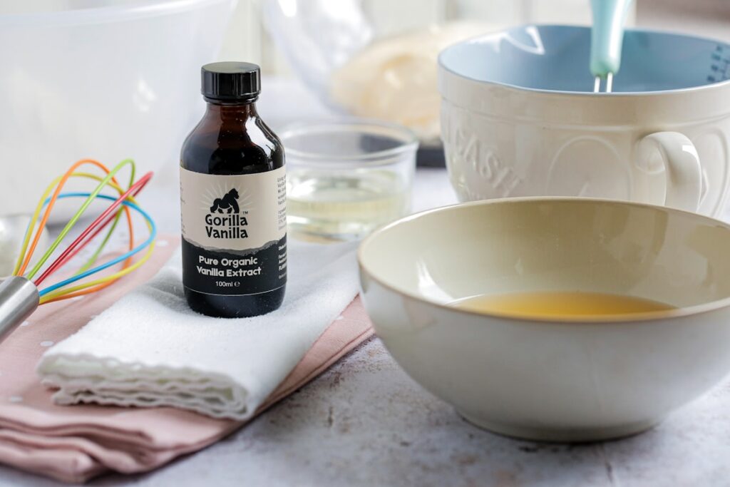 Dark glass bottle of Gorilla Vanilla pure organic vanilla extract on a kitchen counter beside mixing bowls, a whisk, and other baking supplies.