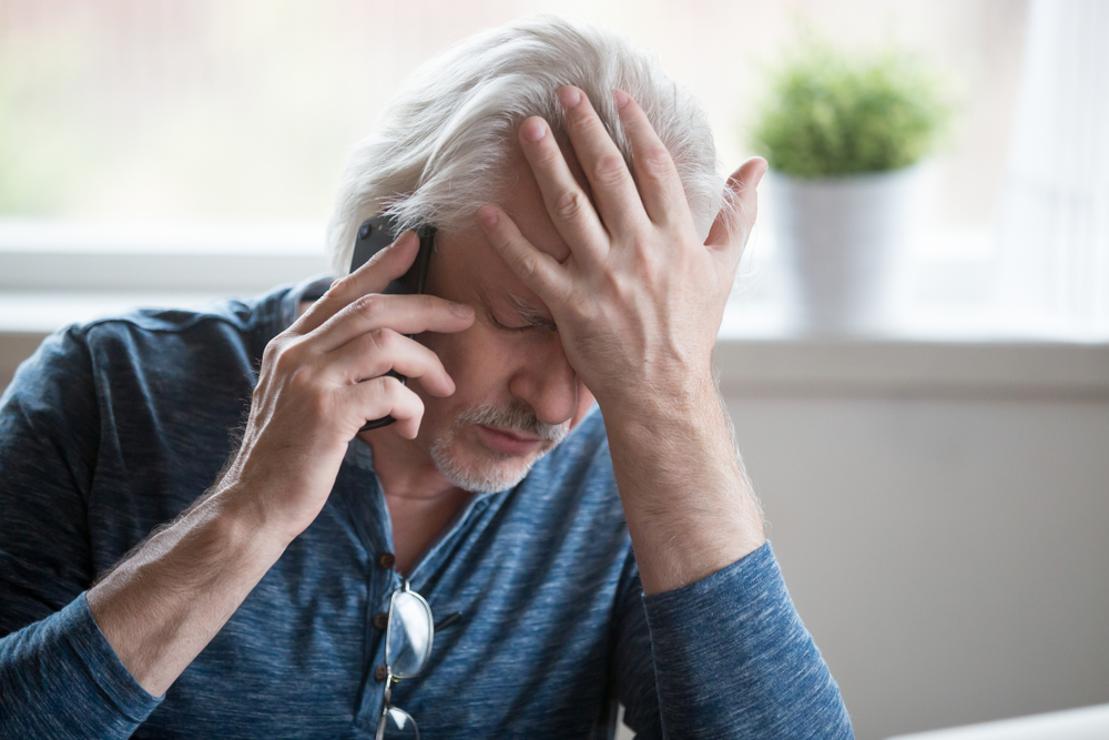 man on phone with hand placed over head in pain
