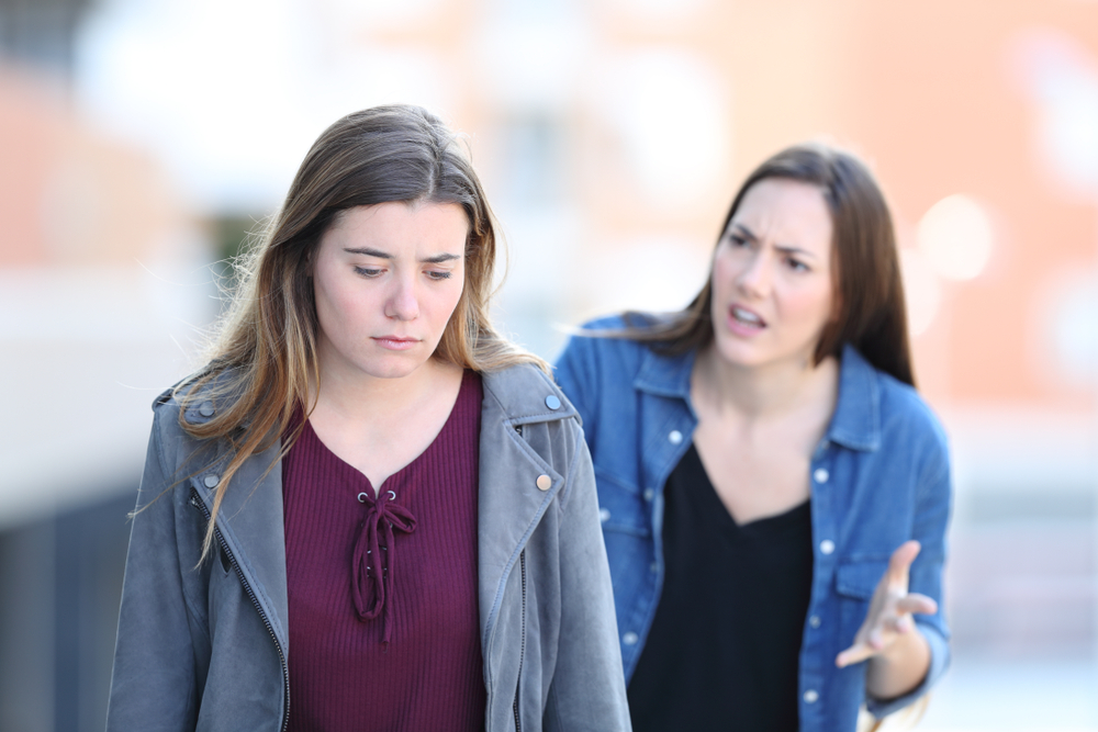 Angry girl scolding her stressed friend walking in the street
