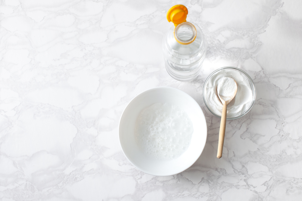 Reaction of baking soda with vinegar in a bowl with a Cup of dry soda, a spoon and a bottle of vinegar. 
