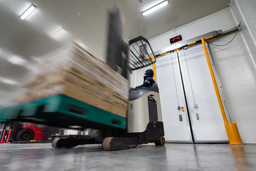 Worker Stand-on stacker truck used to lift and move the ready meals goods stock in cold room or freezer room.