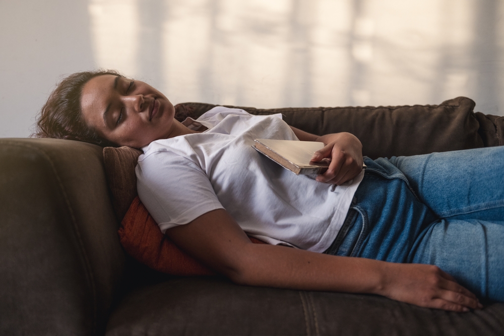 Pretty woman napping on the sofa in her living room after reeding book