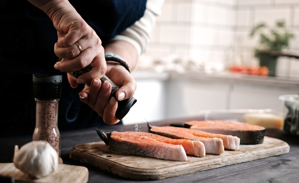 Woman Preparing Healthy Dinner By Salting Raw Red Salmon For Family Cooking