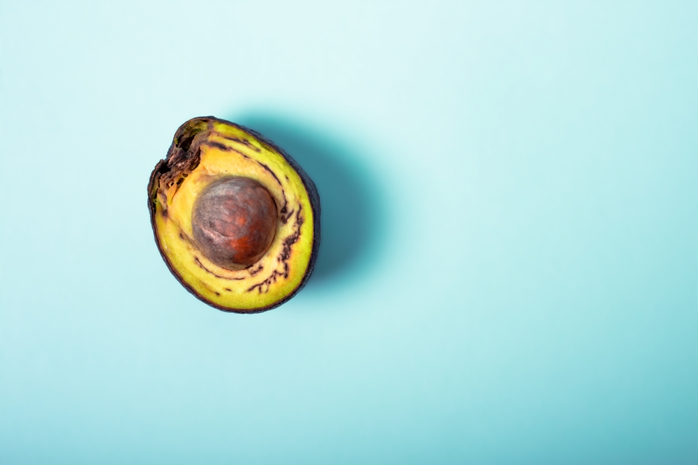 Rotten avocado, overriped, bad avocado. Half sliced fruit, freegan food concept, blue background. The theme of careful consumption and care for the environment. Copyspace