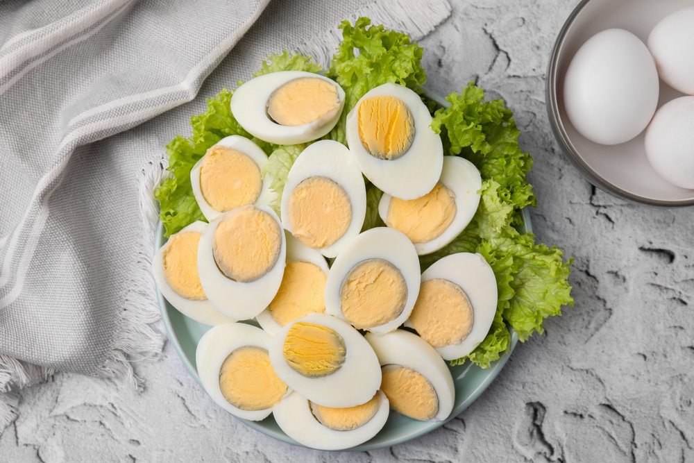 Fresh hard boiled eggs and lettuce on light grey textured table, top view
