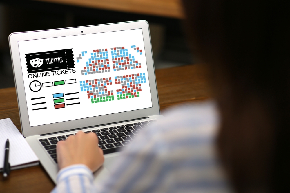 Woman buying theater tickets online via laptop at table, closeup